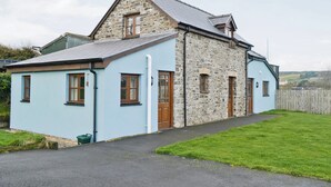 A two-story stone house with a light blue exterior, a sloped roof, and a visible chimney.