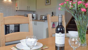 A dining table with a bottle of Jacob's Creek wine, two wine glasses, and a vase with pink flowers.