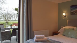 Een hotelkamer met een bed, een tafel met stoelen, een champagnefles en uitzicht op het omliggende landschap.
