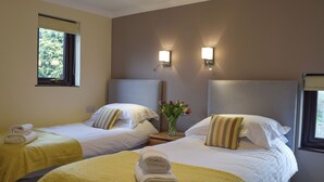 Hotelkamer met twee bedden, elk met hoofdeinde, een nachtkastje met een bloemenvaas en een raam met gordijnen.