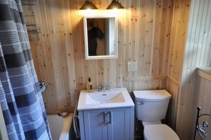 Une salle de bain aux murs lambrissés, avec un lavabo blanc, un miroir et des toilettes.