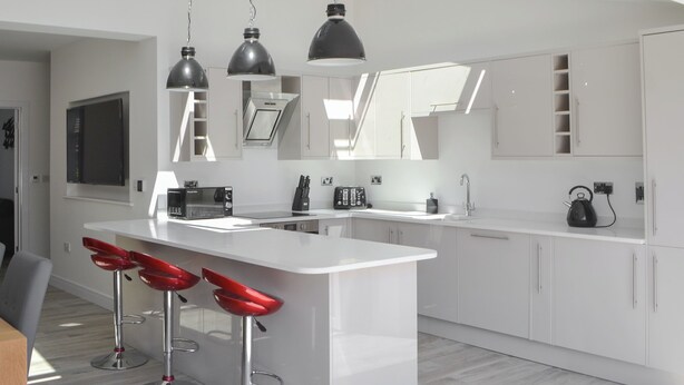 A modern kitchen with white cabinetry, a central island with red bar stools, and pendant lighting. - 3 bedroom accommodation in Amble (Amble)