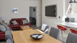 A modern living room with a red leather sofa, a wooden dining table, and a kitchen area with a microwave. - 3 bedroom accommodation in Amble (Amble)