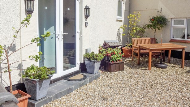 En patio med et bord, stole, plantekasser og en skydedør af glas.