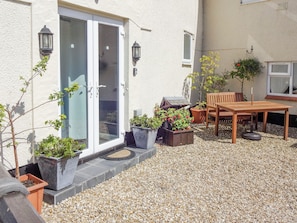 A patio with a table and chairs, potted plants, and a sliding glass door. - 1 bedroom accommodation in Pen-y-Sarn, near Amlwch (Pen-y-Sarn, near Amlwch)