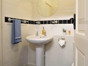 A bathroom with a white sink, a towel hanging on the wall, a mirror, and a small potted plant.