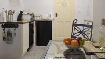Una cocina con una mesa de vidrio, un cuenco de frutas, una copa de vino y una botella de vino.