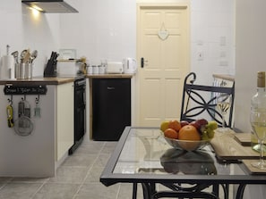 A kitchen with a glass table, a bowl of fruit, a wine glass, and a bottle of wine.