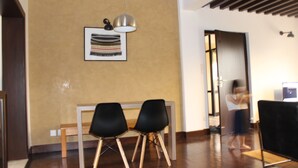 Una habitación con suelo de madera, un banco, dos sillas negras, una obra de arte enmarcada en la pared y una puerta que conduce a otra habitación.