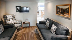 A living room with a sofa, armchair, and a television on the wall. - 4 bedroom accommodation in Mount, near Bodmin (Mount, near Bodmin)