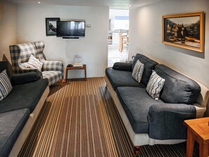 A living room with a sofa, armchair, and a television on the wall.