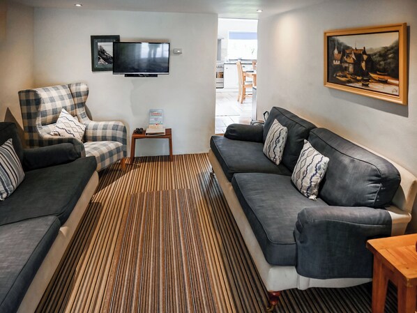 Una sala de estar con sofá, sillón y televisor en la pared.