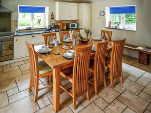 A dining area with a wooden table set for four, surrounded by chairs, with a kitchen in the background. - 4 bedroom accommodation in Mount, near Bodmin (Mount, near Bodmin)