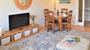A dining area with a round table, chairs, a television, and a vase of flowers. - 2 bedroom accommodation in Beadnell (Beadnell)