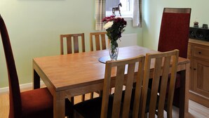 A dining area with a wooden table, chairs, a vase with flowers, a window with curtains, and a radiator. - 3 bedroom accommodation in Oban (Oban)