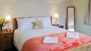 A neatly made bed with white bedding and a red blanket, two bedside lamps, a wooden nightstand, a floral pillow, and a mirror on the wall. - 3 bedroom accommodation in Oban (Oban)