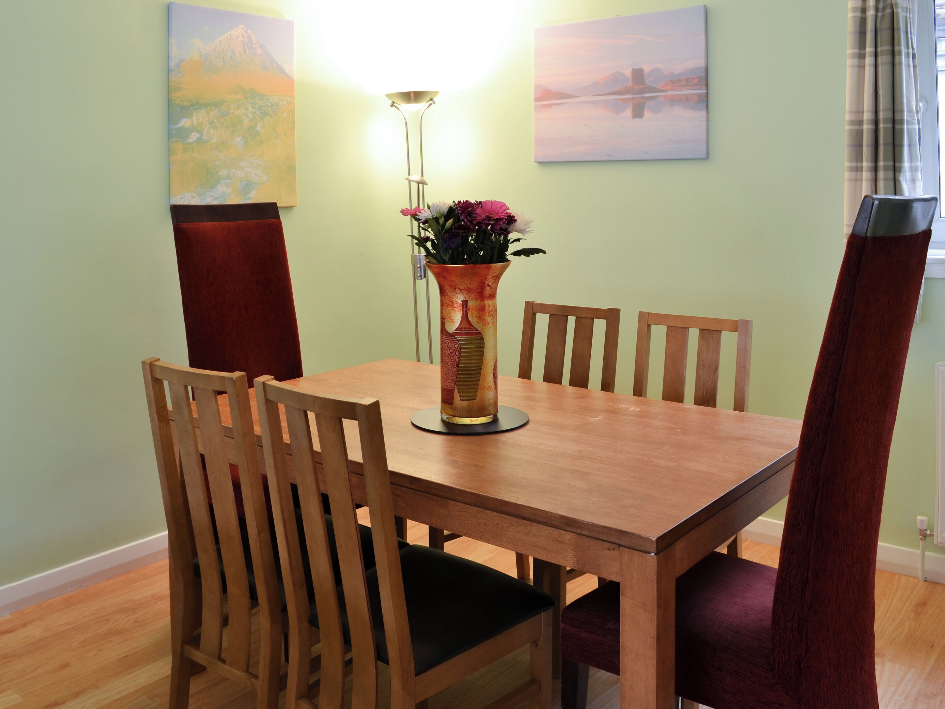 A dining table with four chairs, a vase with flowers, and two paintings on the wall.