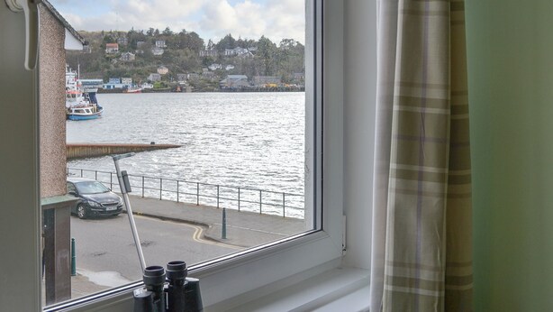 A window with binoculars, a view of a water body, a dock, and a building across the water. - 3 bedroom accommodation in Oban (Oban)