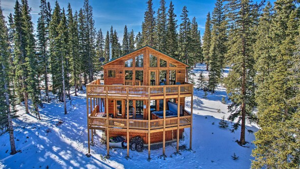 Une cabane en bois dotée d’un balcon, entourée de neige et de pins.