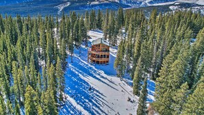 Un chalet entouré de paysages enneigés et de grands pins, avec une chaîne de montagnes en arrière-plan.