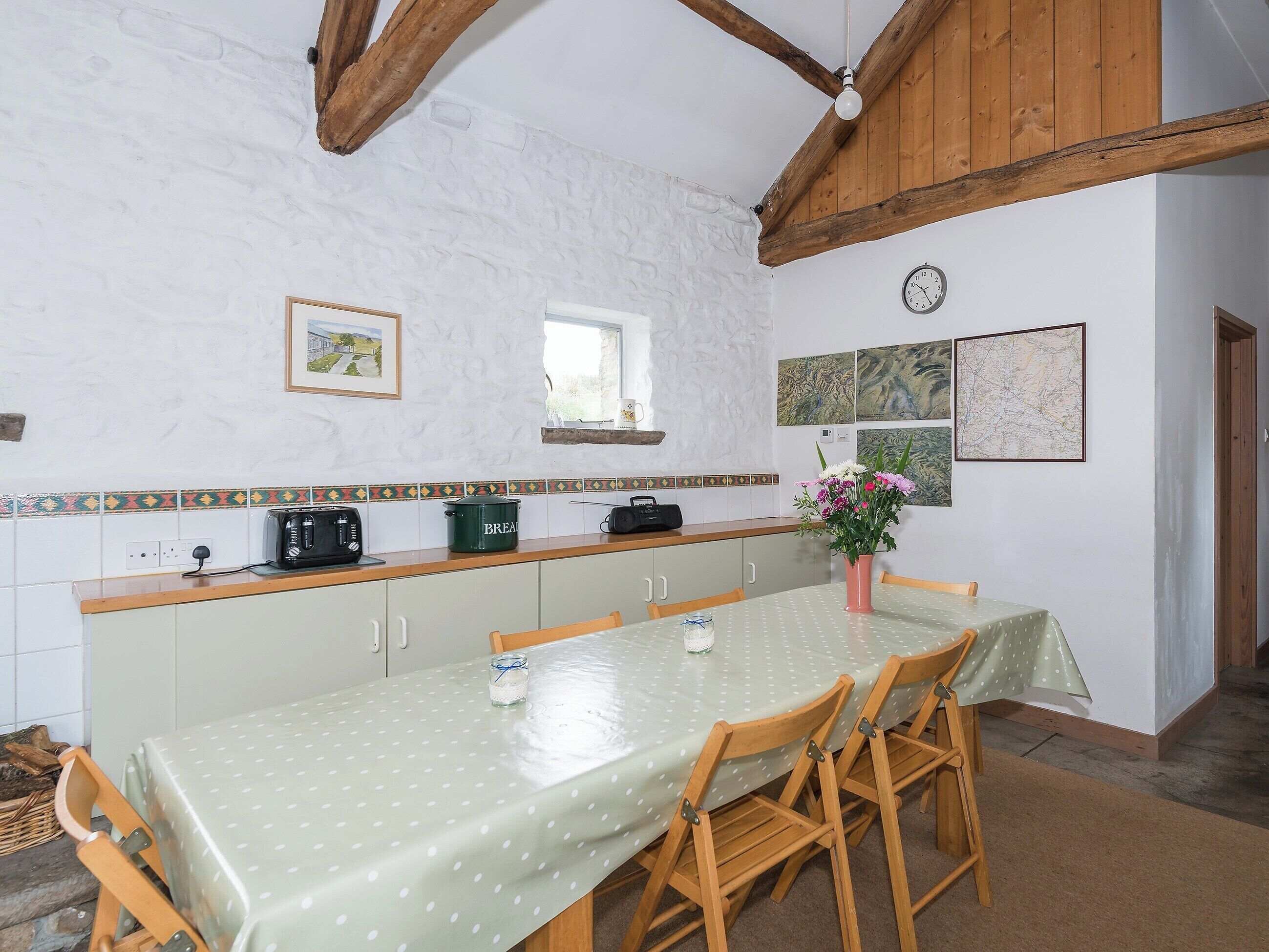 Una cucina con soffitto in legno, pareti bianche, zoccolo di piastrelle, una finestra e un tavolo da pranzo con sedie.
