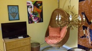 A room with a television on a wooden cabinet, a hanging chair with a pink cushion, a chandelier, and two framed artworks on the wall. - Relax as a couple on the large terrace, view of the mountains, Wi-Fi (Mogan)