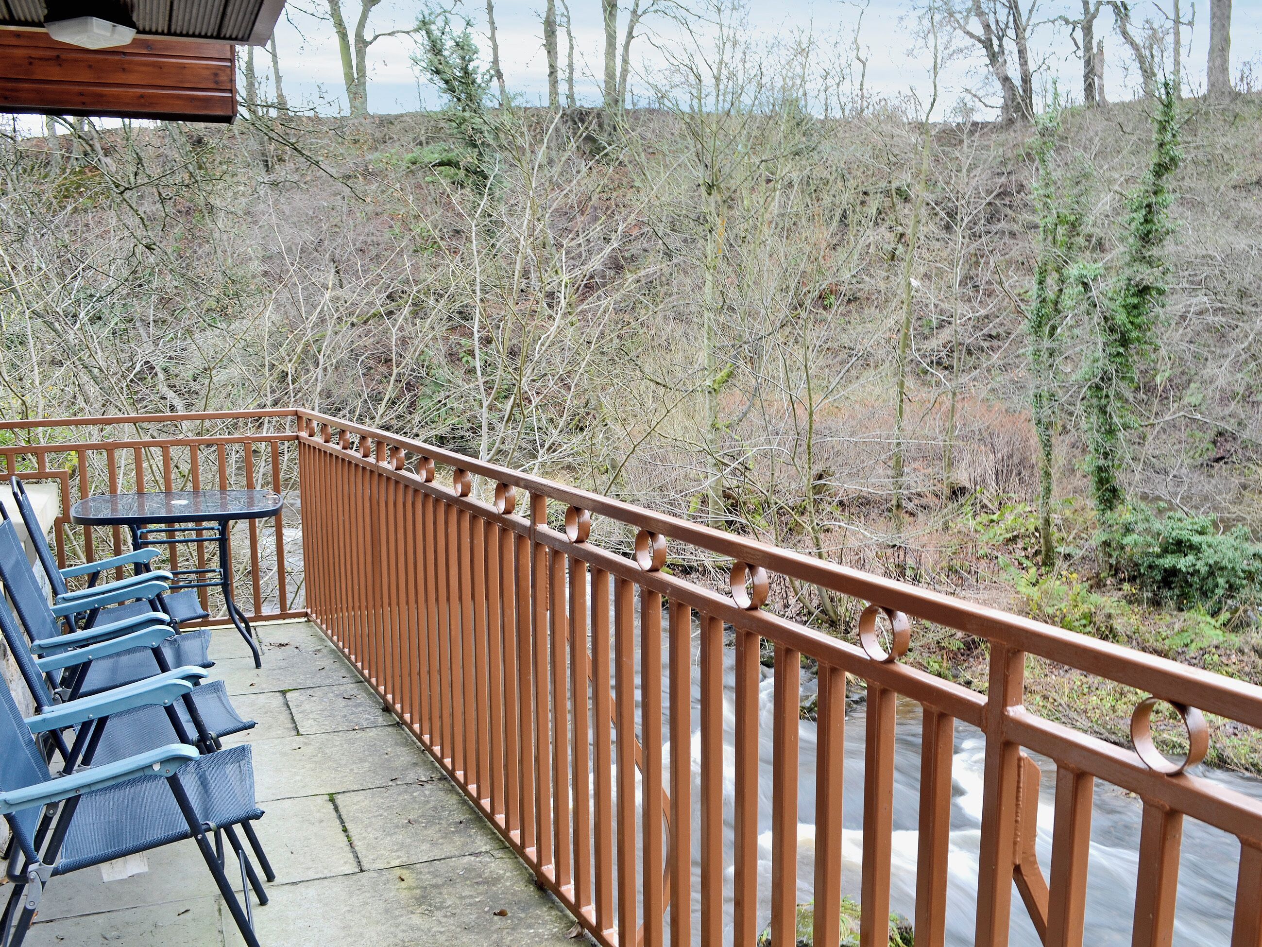 A balcony with a metal railing, a table, and blue chairs.