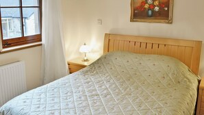 Un dormitorio con cama, mesita de noche, lámpara, ventana y un cuadro en la pared.