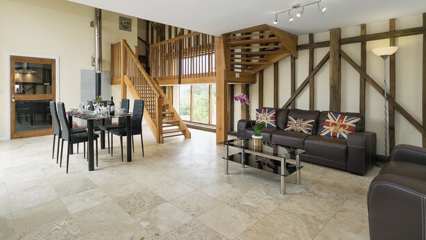 Un vaste espace de vie agrémenté d’un escalier en bois, d’une table à manger avec des chaises et d’un canapé orné de coussins décoratifs.