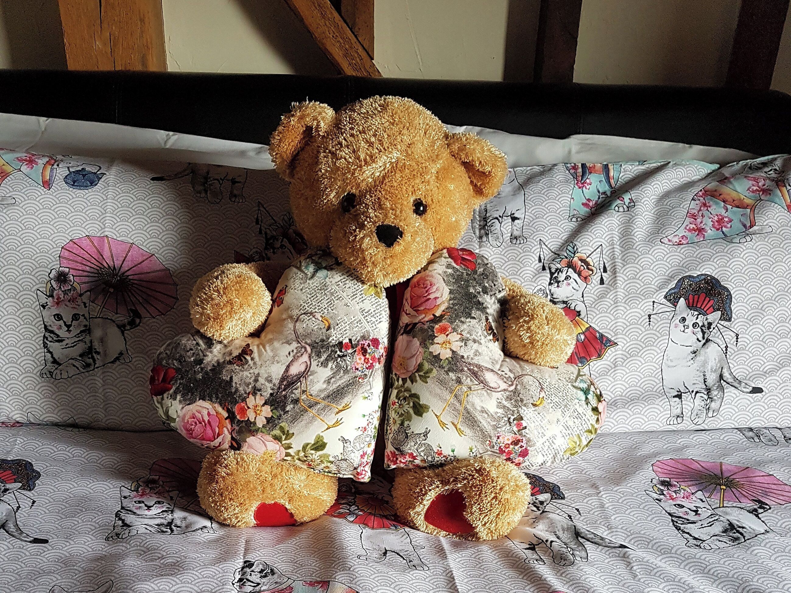 A teddy bear sitting on a bed with a floral patterned bedspread.