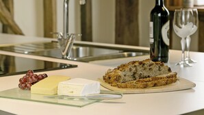 Un plan de travail de cuisine avec une miche de pain, du fromage, des raisins, une bouteille de vin et un verre à vin.