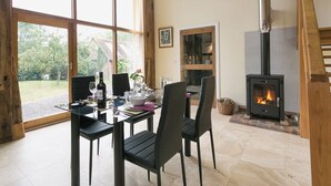 Un coin repas avec une table dressée pour quatre personnes, une cheminée et de grandes fenêtres donnant sur l’extérieur.