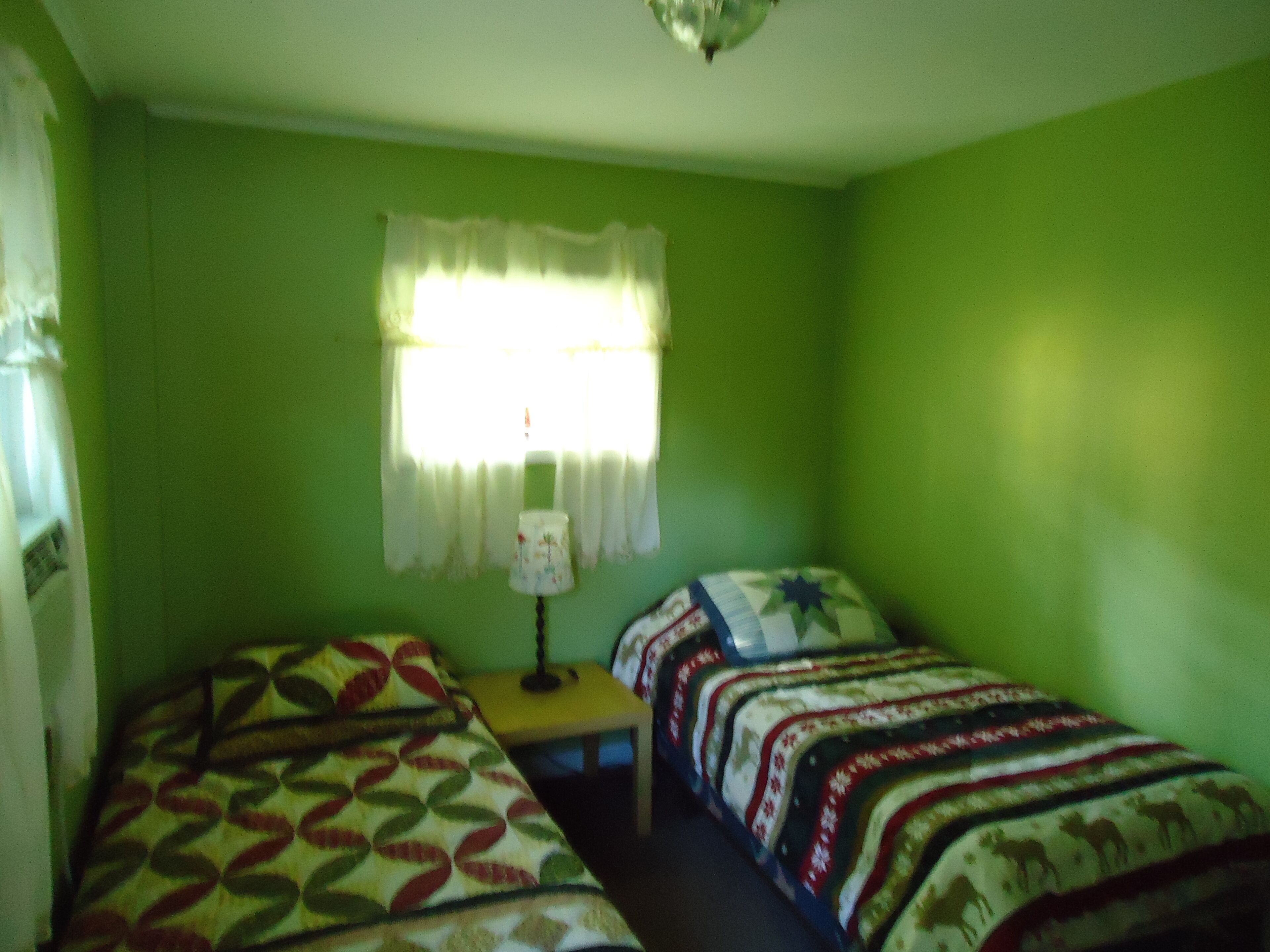 A room with two beds, a window with curtains, and a lamp on a nightstand.