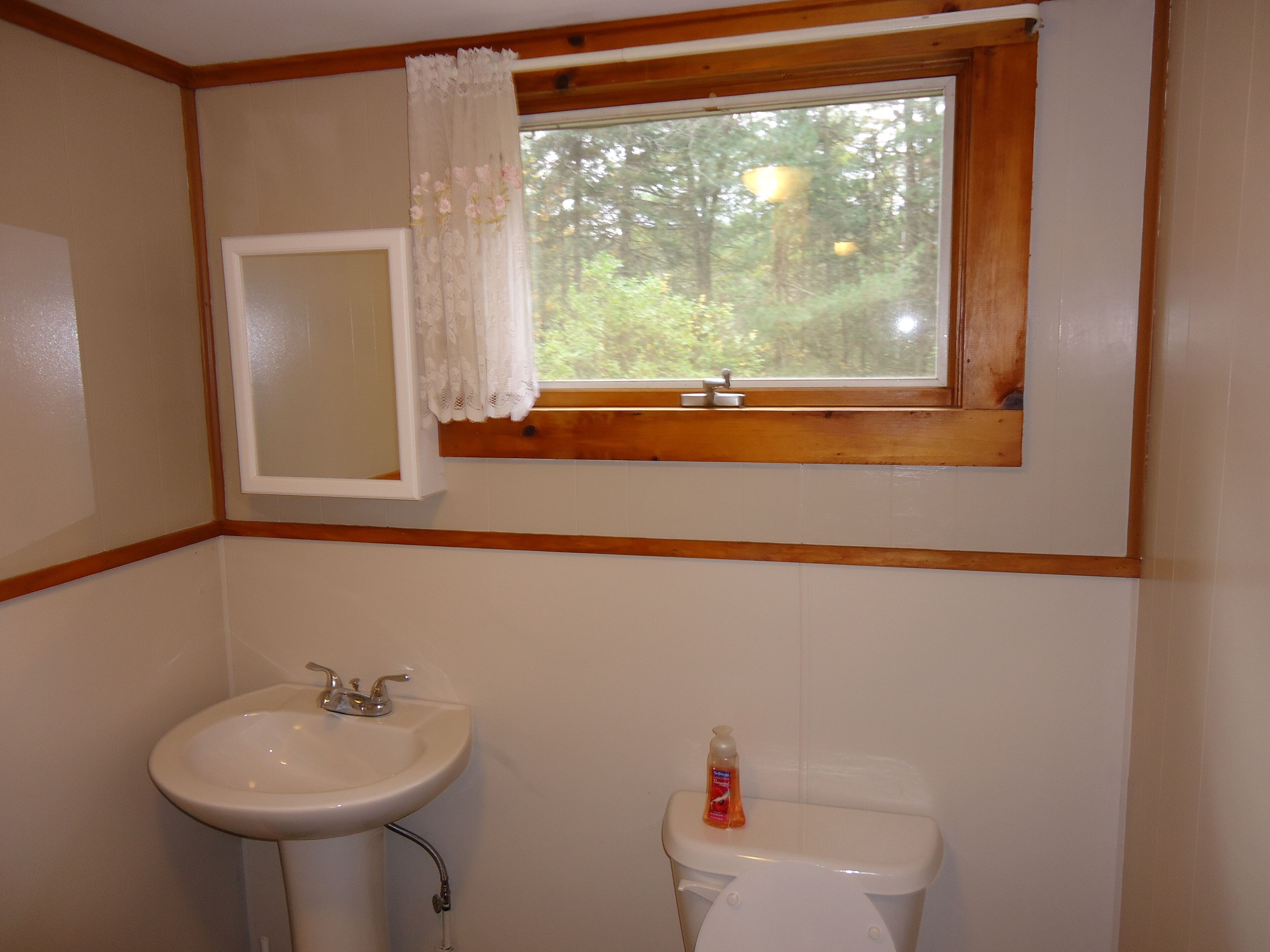 A bathroom with a sink, toilet, and a window with a wooden frame and lace curtain.