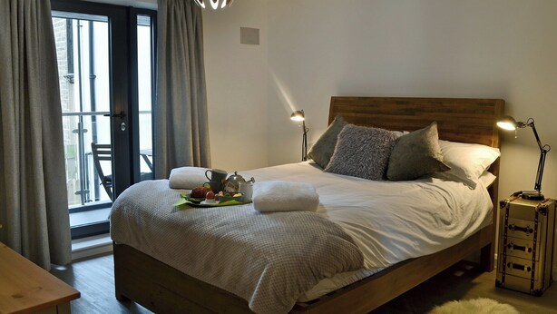 A neatly made bed with pillows, a bedside table with a lamp, and a view of the outdoors through a window. - 2 bedroom accommodation in Alnwick (Alnwick)