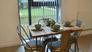 A dining table set for four with metal chairs, a view of a garden through a window, and framed pictures on the wall. - 2 bedroom accommodation in Alnwick (Alnwick)