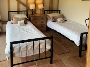 Two single beds with black frames, a wooden nightstand with two lamps, and a tiled floor.