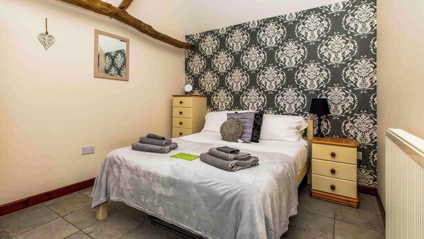 A bedroom with a bed, bedside tables, a dresser, a mirror, and a patterned wallpaper. - Thyme for a relaxing break for two. (Catfield)
