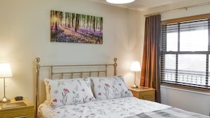 Een slaapkamer met een bed, twee nachtkastjes, een lamp, een schilderij, een raam met gordijnen en een plafondlamp.