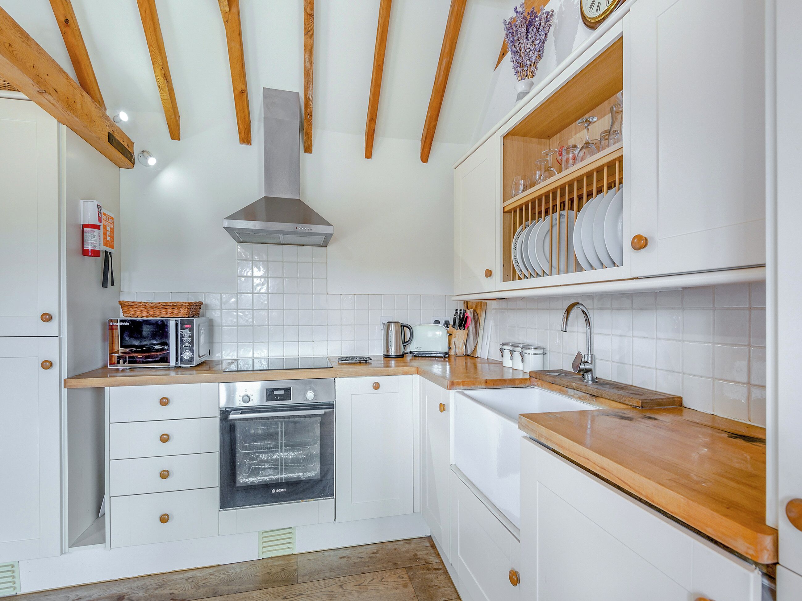 Una cocina con armarios blancos, vigas de madera, un horno Bosch y un lavamanos con encimera de madera.