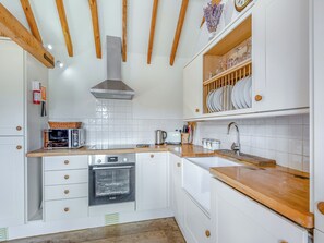 A kitchen with white cabinetry, wooden beams, a Bosch oven, and a sink with a wooden countertop.
