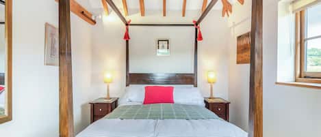 Una cama con dosel, un cabecero de madera, dos mesitas de noche con lámparas y una ventana a la derecha.