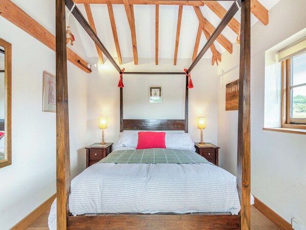 A four-poster bed with a wooden headboard, two bedside tables with lamps, and a window on the right.