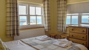 A bedroom with a bed, a dresser, and two windows with curtains. - Captains Cottage - E3643 (Whitby)