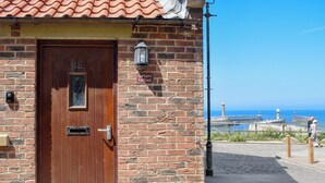 A brick cottage with a wooden door, a mailbox, and a sign reading "Captain's Cottage". - Captains Cottage - E3643 (Whitby)
