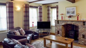 A living room with a fireplace, leather sofas, a television, and plaid curtains. - Captains Cottage - E3643 (Whitby)