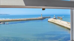 A coastal view with a pier extending into the water, a lighthouse, and a stone wall. - Captains Cottage - E3643 (Whitby)