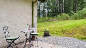 Eine Terrasse mit Tisch und Stühlen, einem Blumentopf und einem Rasen mit Bäumen im Hintergrund.