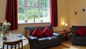 Ein Wohnzimmer mit einer Couch, einem Esstisch für zwei Personen und einem Fenster mit Vorhängen.