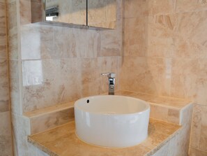 Ein Badezimmer mit einem weißen Waschbecken, einem Spiegel darüber und beige gefliesten Wänden.